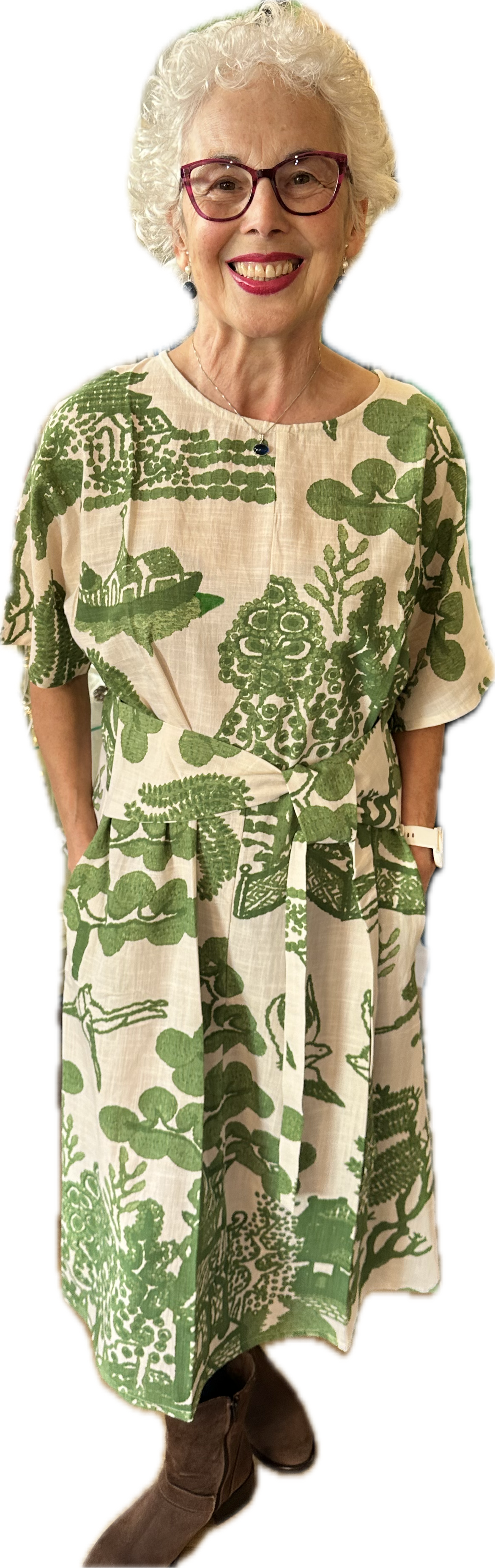 Smiling older woman wearing green willow print dress posing indoors against plain white background
