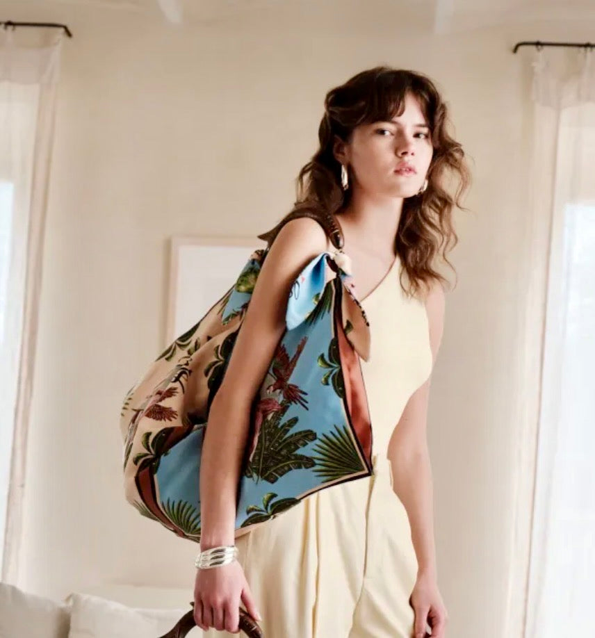 Alex Max satin style tote bag with tropical print and fish-shaped wooden handle carried by woman in light outfit
