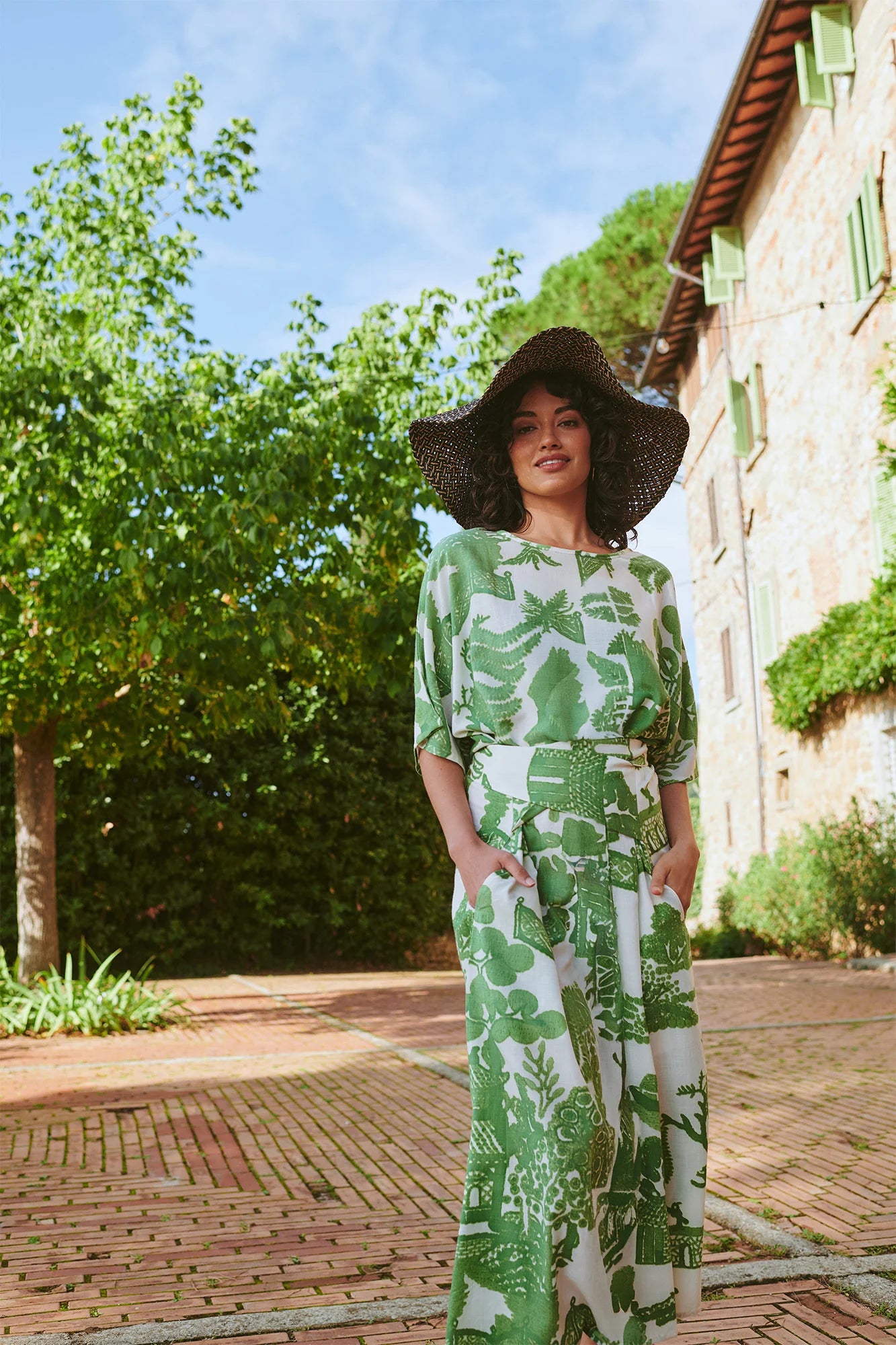 Woman wearing One Hundred Stars dress with green willow print and wide belt outside with large sun hat