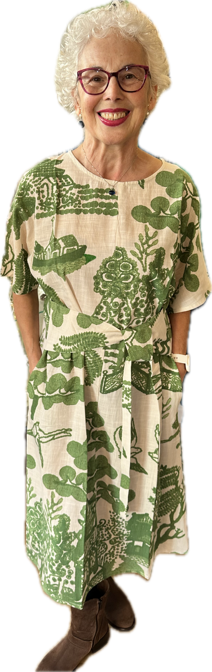 Smiling older woman wearing green willow print dress posing indoors against plain white background
