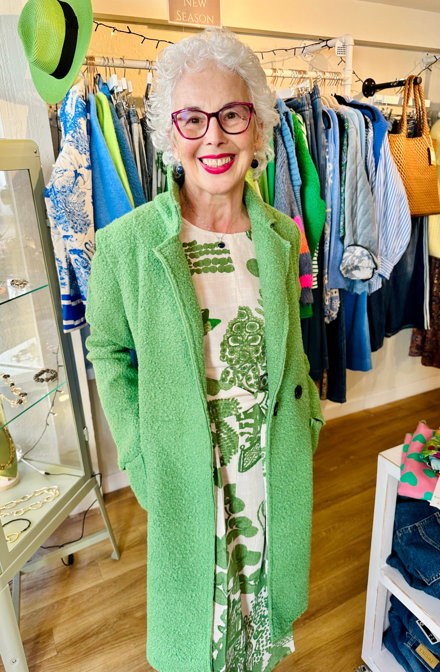 Older woman smiling indoors wearing green willow print dress with bright green textured coat