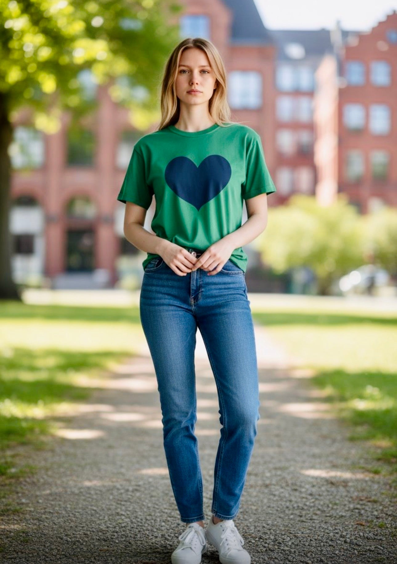 Woman wearing a green t-shirt with a large navy blue heart graphic, paired with blue jeans and white sneakers, outdoors in park